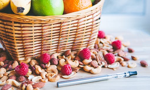Silver vape pen on table next to fruit bowl and nuts