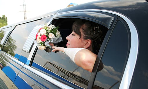 Bride holding bouquet with head out the window of limousine