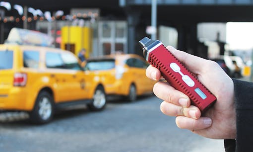 Hand holding cannabis vaporizer with New York City cabs on street in background