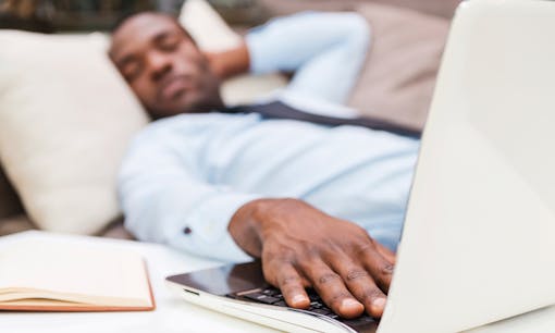 A man sleeping on a couch behind a laptop