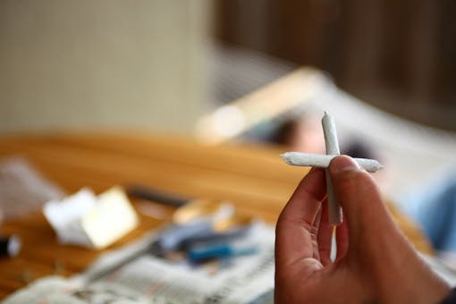 Hand holding cannabis "cross joint" in living room