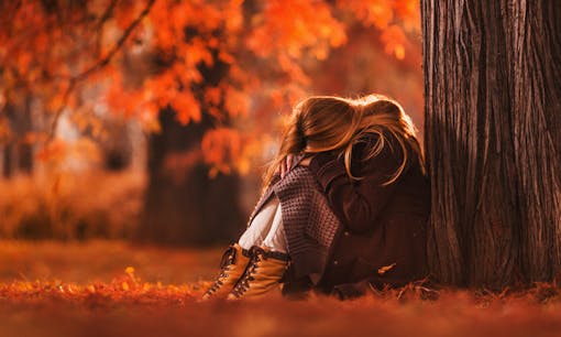 Girl hanging head down in park with beautiful autumn leaves in background