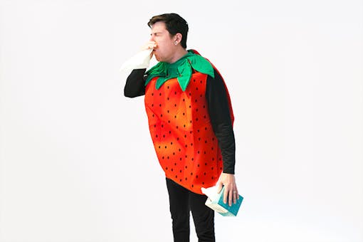 Man wearing strawberry costume coughing into tissue