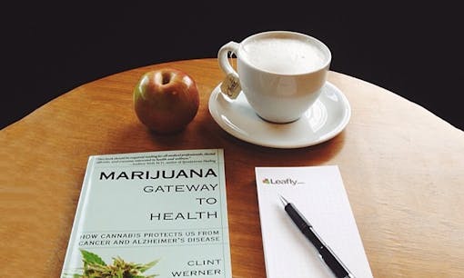 Table with coffee, an apple, a "Marijuana: Gateway to Health" book, and a Leafly notepad