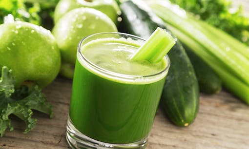 Glass of green juice near green vegetables
