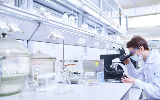 Young scientist examining sample with microscope in modern laboratory.