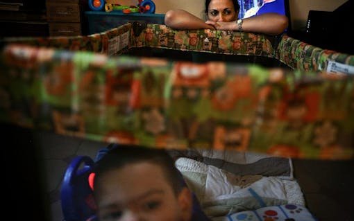 While Bruno Stillo moves about in his playpen, his nurse Idania Gonzalez takes a brief rest while watching over him in their Miami, FL home on Friday, October 28, 2016. When his mother isn't watching over him, Gonzalez is always watching to make sure he's safe. (Scott McIntyre for Leafly)