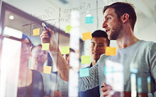 Cropped shot of coworkers using sticky notes on a glass wall during a meeting