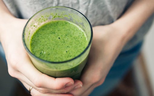 woman holding a glass of green smoothie