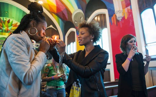 Chicago resident Andrea Camp, from left, gets a light from Lakewood resident Kimm Miller, as Mia Jane smokes at a private viewing on opening day of the International Church of Cannabis. (Daniel Brenner for Leafly)