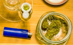 Lighter sitting next to weed jar and fresh bowl on light wood background