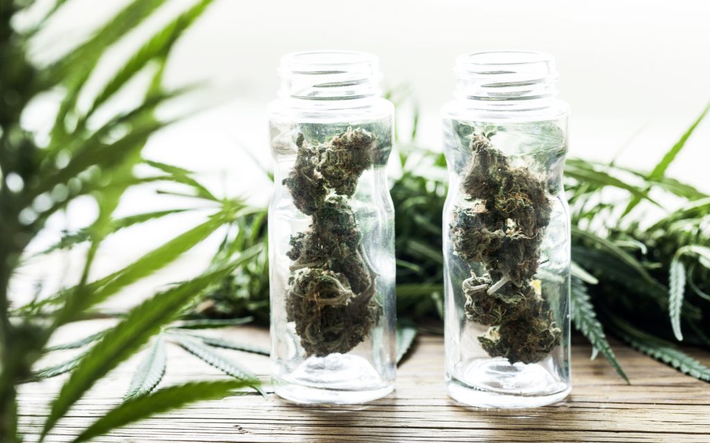 Marijuana buds in small glasses on wooden table with cannabis leaves