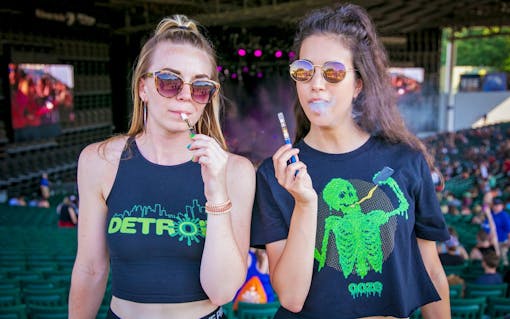 two women using ooze vape pens at a festival