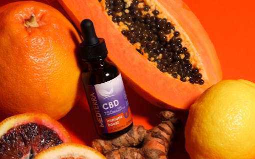 Medterra CBD Immune Boost tincture bottle laying amongst citrus fruits and papaya