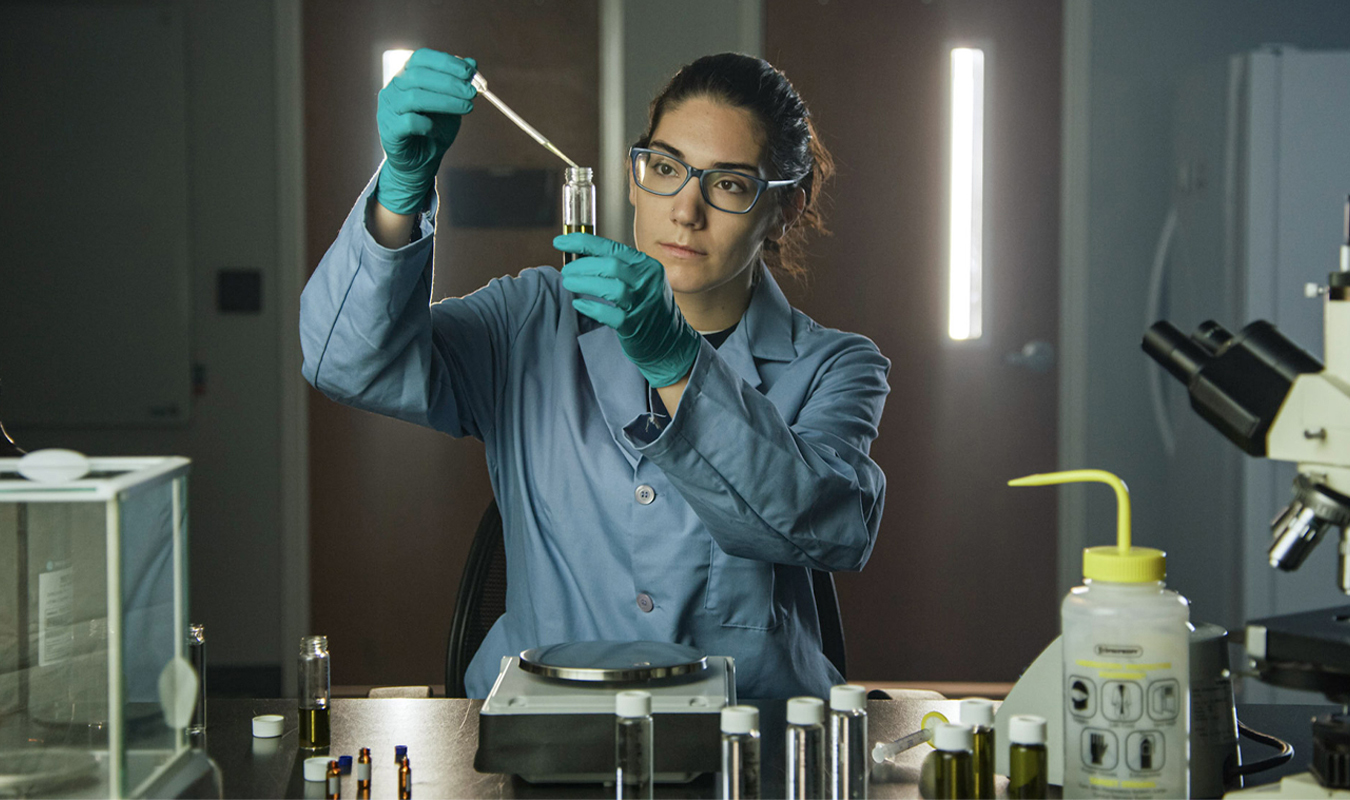Female scientist in protective gear working with a medical dropper in a lab