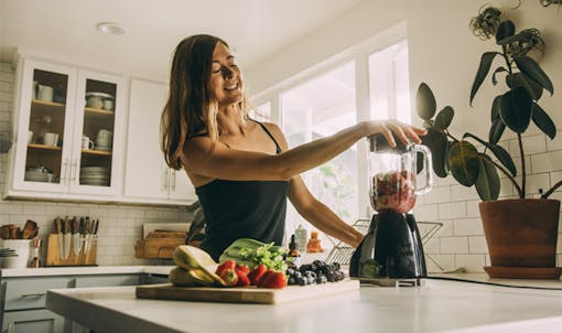 Woman making smoothie in her kitchen with fresh fruits and vegetables
