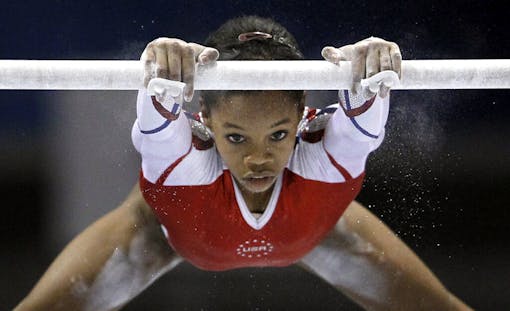 Gabby Douglas swinging from gymnastic bar.