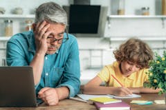 exhausted dad watching his child do homework at the kitchen table