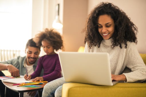 Mother searching on computer with father and child in the background playing