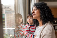 Smiling mother and daughter looking out the window at home