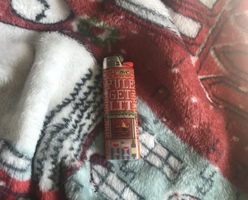 Photo of a lighter reading "Yule Get Lit" laying on a Christmas blanket