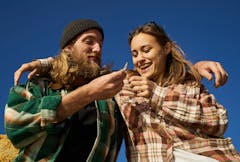 couple of cheerful hipster friends passing joint outdoors on a sunny day