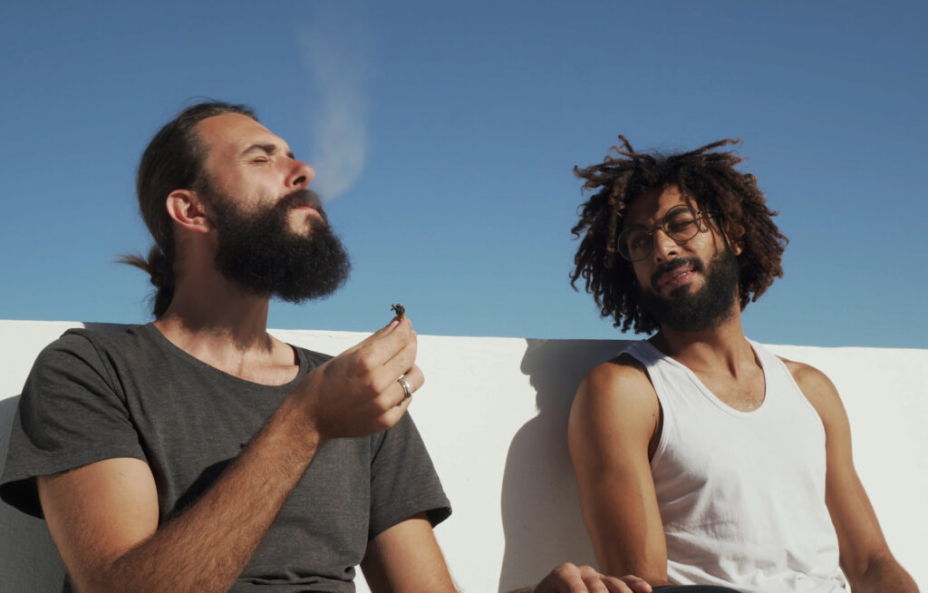 Multiracial friends having fun and smoking weed on blue sky rooftop background