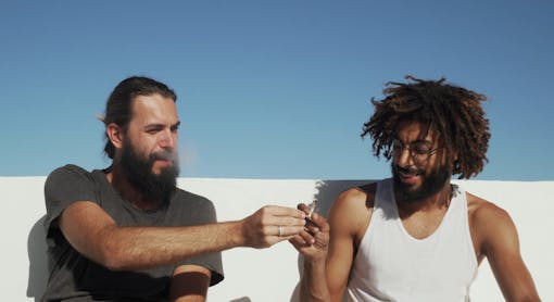 Multicultural friends give each other a joint with weed at rooftop blue sky