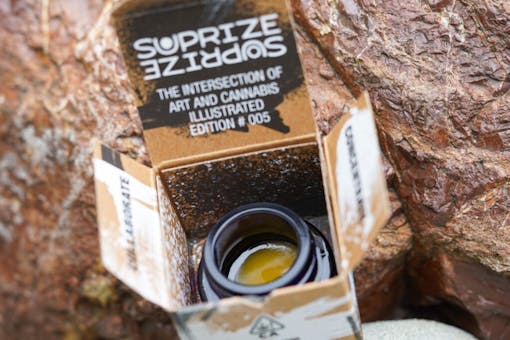 A one-gram jar of amber Suprize Suprize Vanilla Frosting collab in an open box set amid rocks. (Courtesy Suprize Suprize)