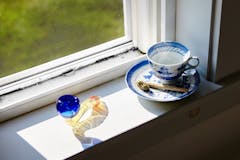 A high angle shot of a marijuana blunt and dry cannabis on a coffee cup near the window