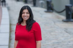 Shaleen Title smiling in a red dress in front of outdoor setting
