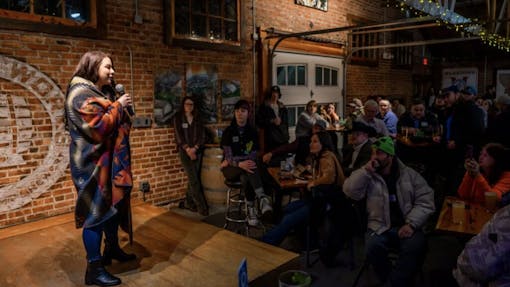 a young woman in a huge coat introduces herself to the crowd at the Lovers Cup
