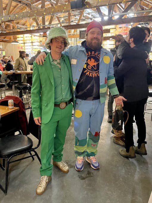 A man in a full green Leprechaun style suit and a man in baby blue suit hugging and smiling at Draught Works brewery at the end of the Lovers Cup