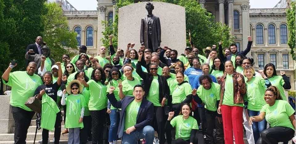 A motley crowd, all wearing bright green T-shirts, many with fists raised, smiles outside in front of a statue of Abraham Lincoln