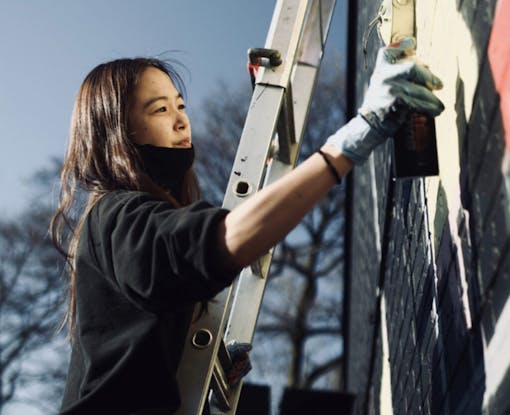 young South Korean woman on a ladder spray paints a wall
