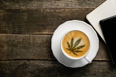 Cannabis coffee - marijuana leaf on coffee foam, rustic wood background