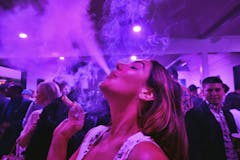 young woman exhales smoke at an indoor party with purple lighting