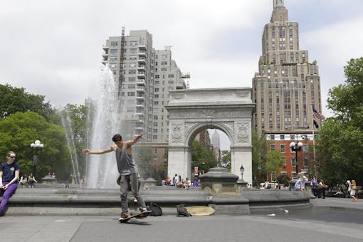 man on skateboard in front of fountain with skyscrapers behind him