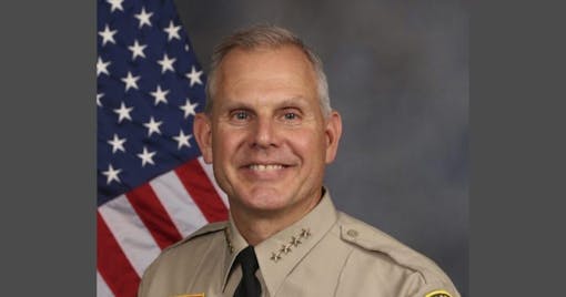 smiling older man with gray hair in uniform next to American flag