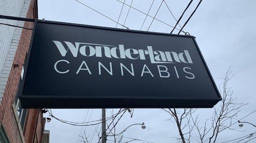 black exterior sign for Wonderland Cannabis sticking out perpendicular to brick wall