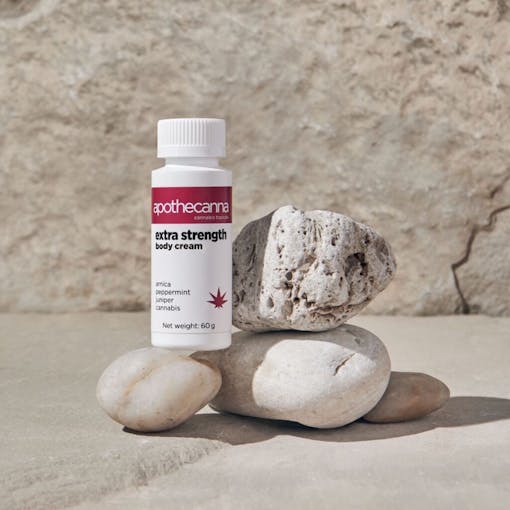 A bottle of Apothecanna's body cream set up with small stones
