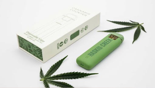 green disposable vape cart next to packaging, with pot leaf displayss