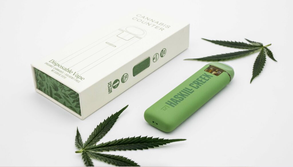 green disposable vape cart next to the packaging, with pot leaf displays