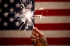 hand holding sparkler in front of American flag