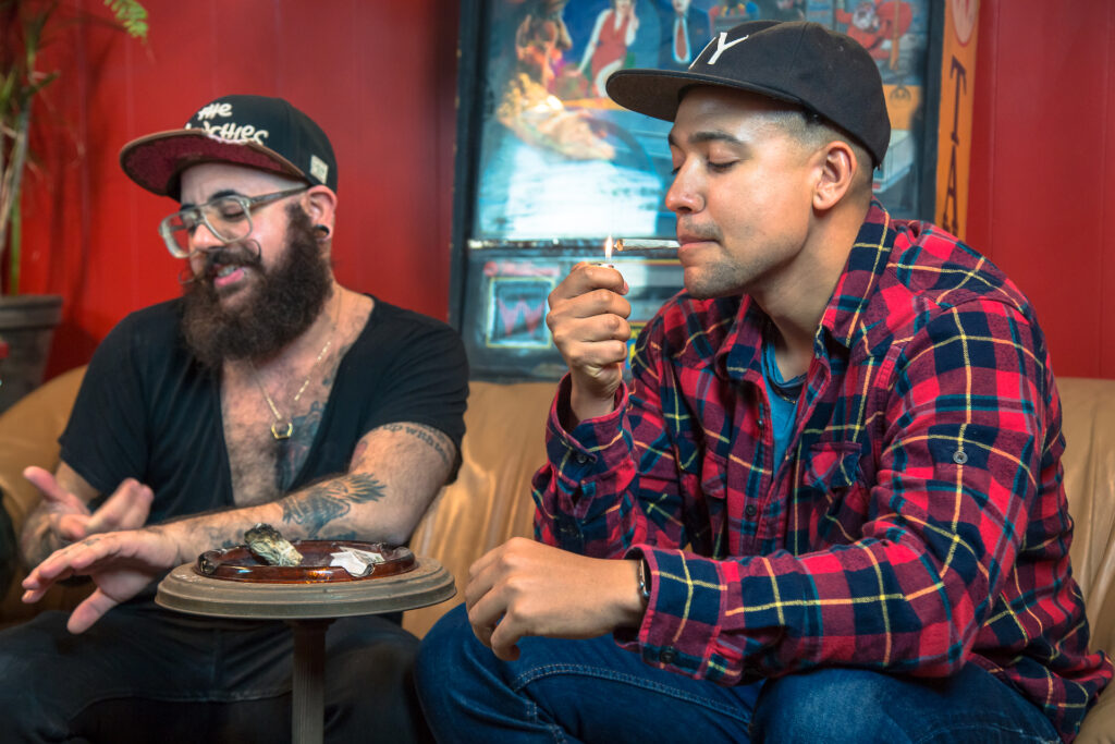 Two people enjoy cannabis while sitting on a couch