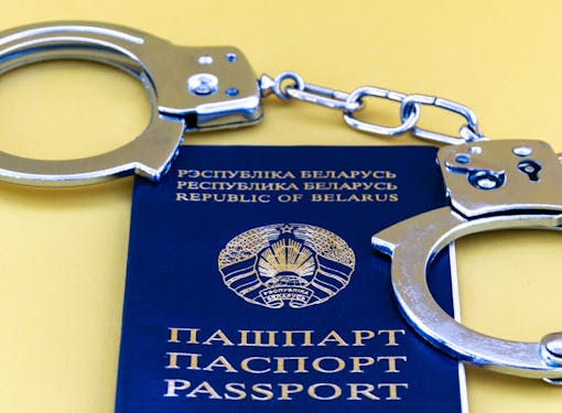 Passport proving the identity of a citizen of the Republic of Belarus and steel handcuffs on a yellow background. Close-up.