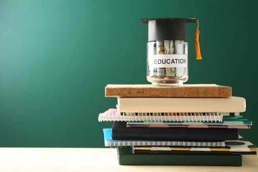 School supplies and glass jar with money for education on wooden table against green background