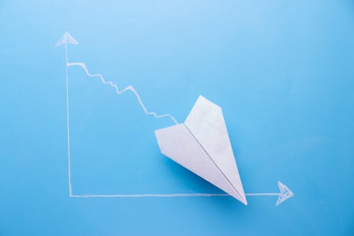 paper plane heading in a downward direction on a blue graph showing a decline