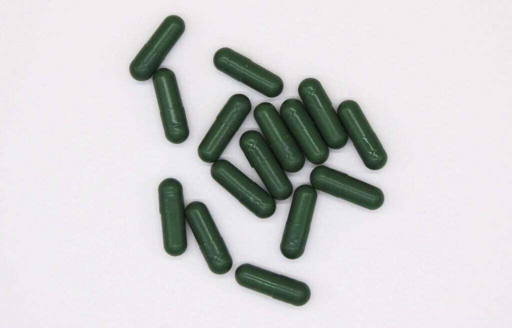 15 dark capsules scattered against a white background