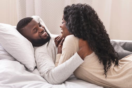 Smiling african american couple having fun in bed, embracing and flirting with each other, closeup